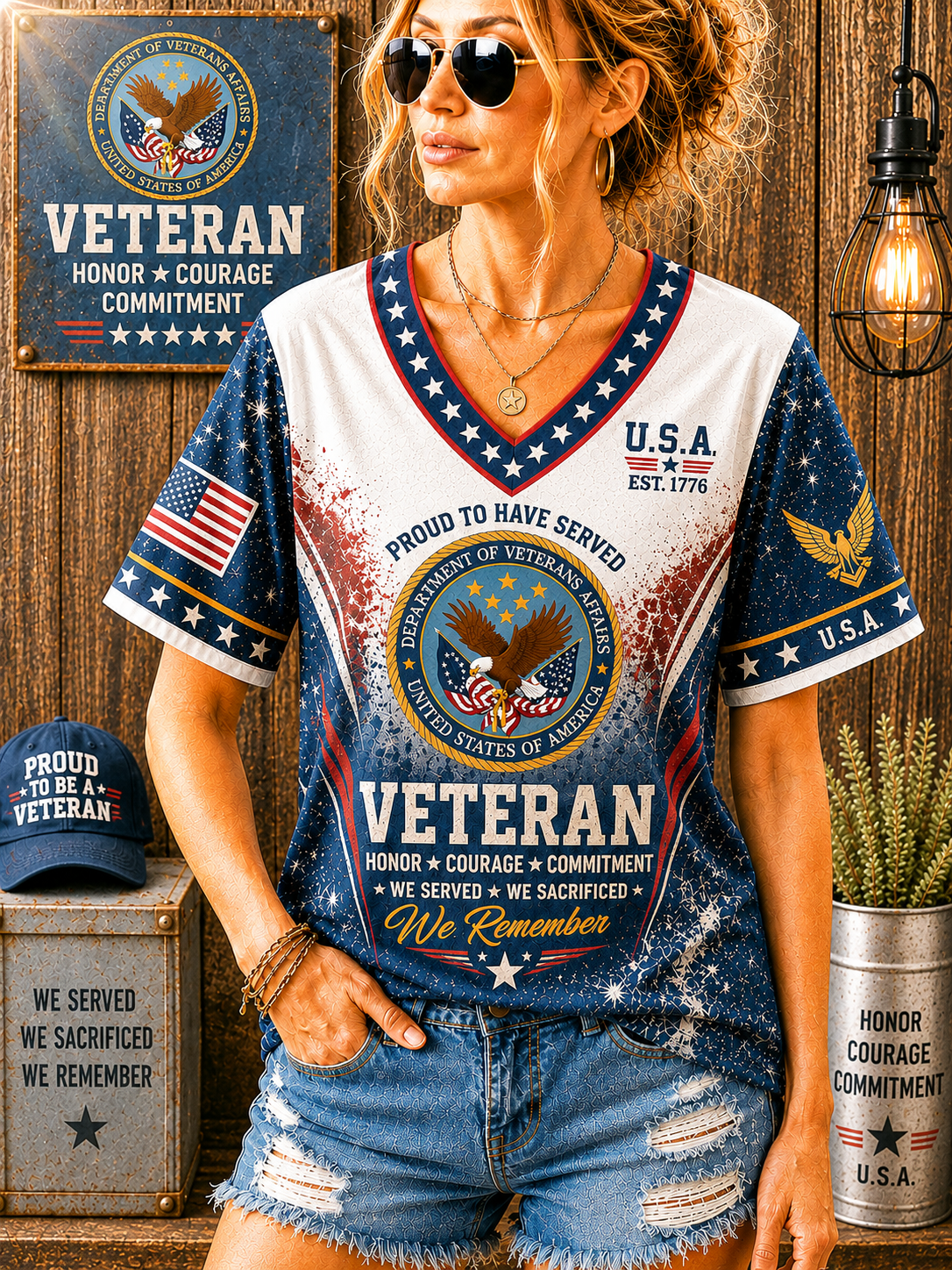 A woman wearing a patriotic 'Veteran' graphic t-shirt with a distressed blue and white design, featuring the US Army emblem and text. She is posing in front of a rustic wooden wall decorated with matching patriotic props, including a hat, a sign, and a light bulb.