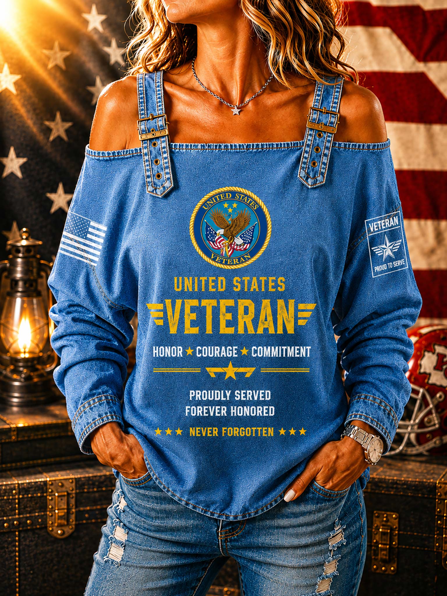 A woman wearing a blue off-the-shoulder long-sleeve top with a distressed denim look, featuring a 'United States Veteran' graphic on the front, posed in front of an American flag and a vintage lantern.