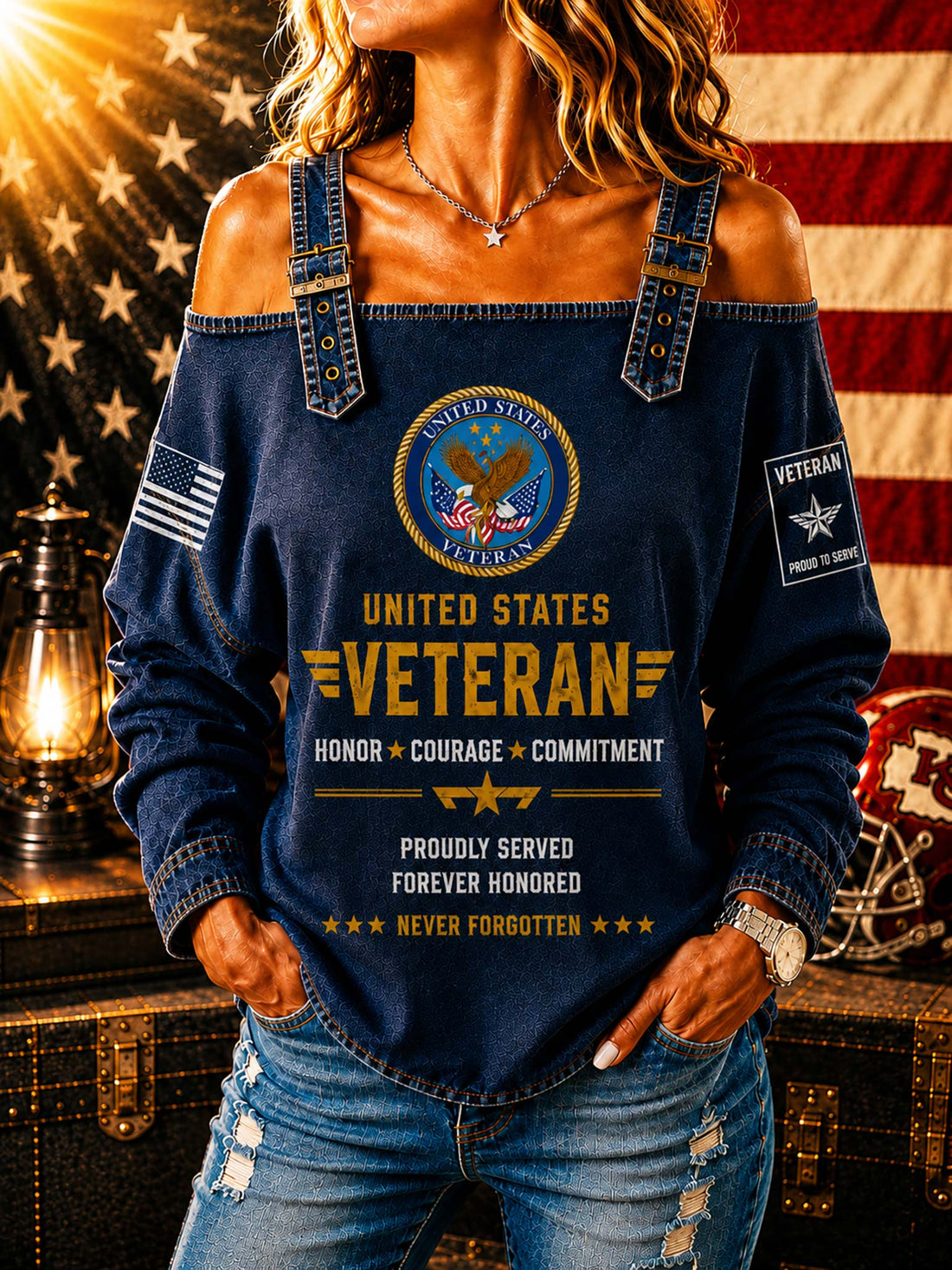 A woman wearing a blue off-the-shoulder long-sleeve top with a distressed denim look, featuring a 'United States Veteran' graphic on the front, posed in front of an American flag and a vintage lantern.