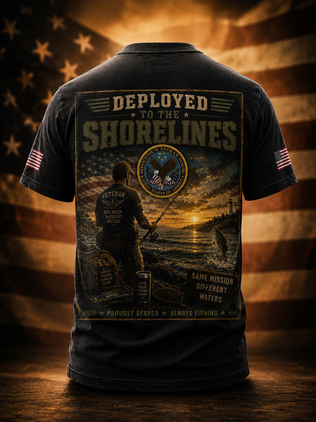 A black short-sleeve t-shirt shown from the back, featuring a large graphic print with a military fishing scene, the text 'DEPLOYED TO THE SHORELINES,' and a circular emblem. The shirt is displayed against a warm, blurred American flag background with a wooden surface below.