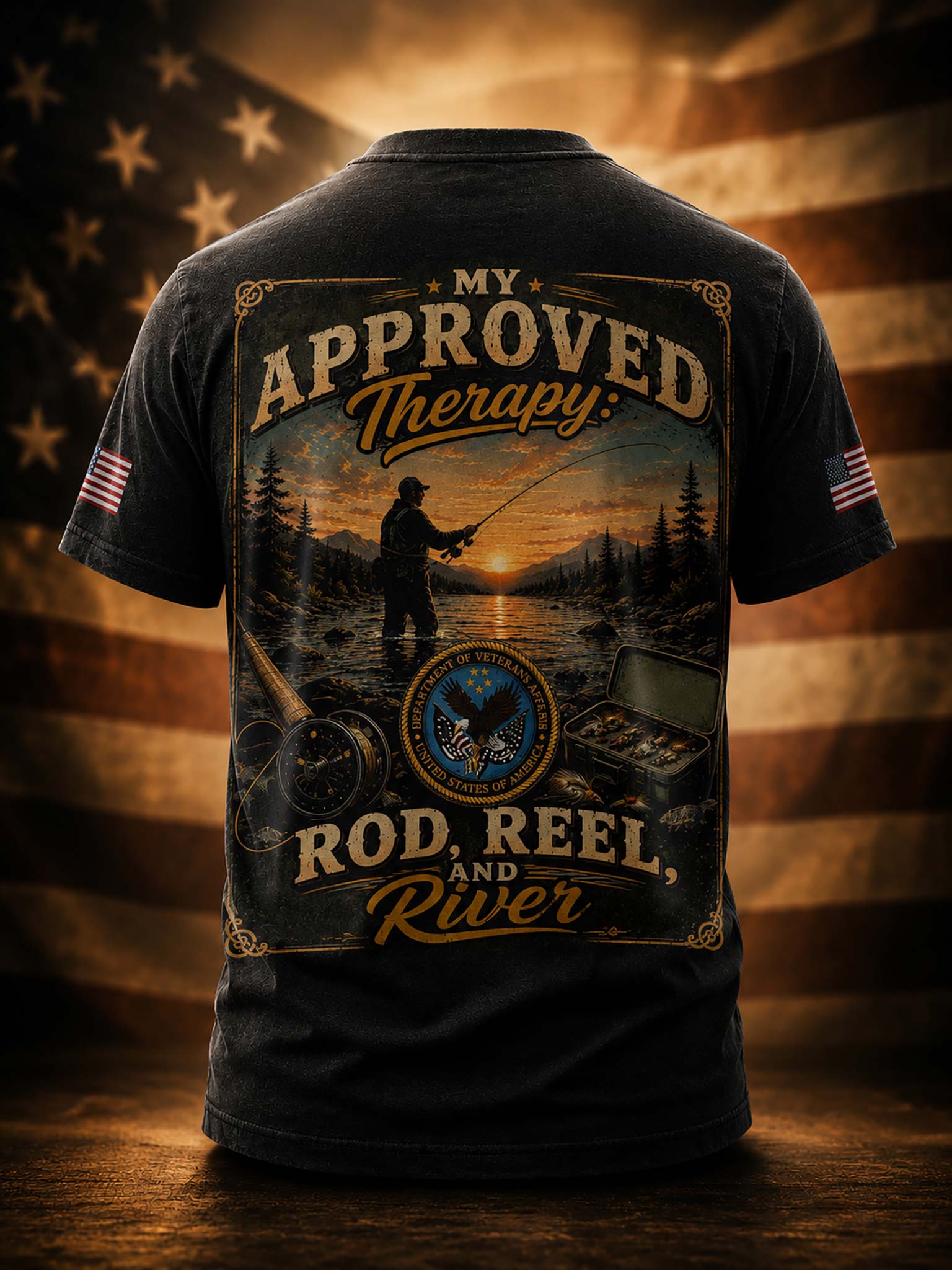 A black short-sleeve t-shirt shown from the back, featuring a large vintage-style fishing graphic with the text 'MY APPROVED Therapy: ROD, REEL, AND River'. The shirt is displayed against a warm-toned American flag background with a wooden surface below.