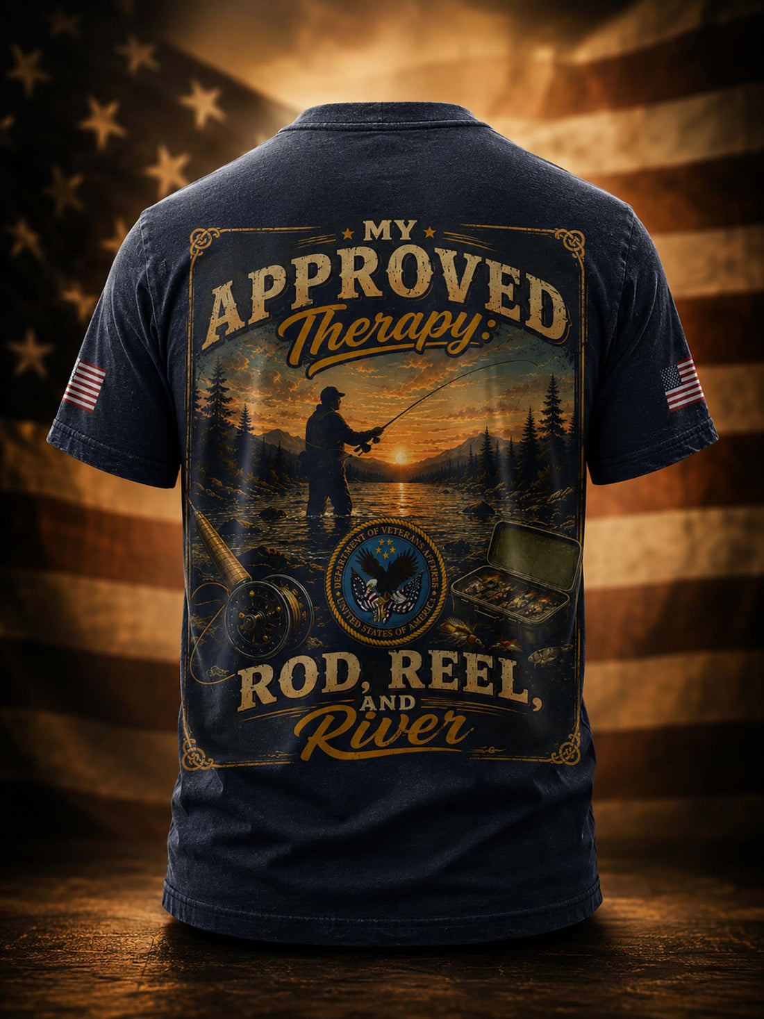 A black short-sleeve t-shirt shown from the back, featuring a large vintage-style fishing graphic with the text 'MY APPROVED Therapy: ROD, REEL, AND River'. The shirt is displayed against a warm-toned American flag background with a wooden surface below.