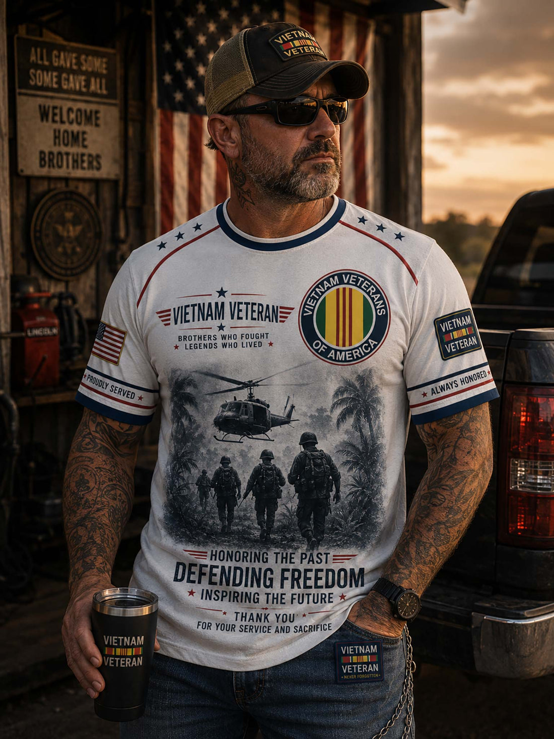 A white short-sleeve t-shirt with a detailed graphic print celebrating Vietnam Veterans. The design features a black-and-white illustration of soldiers and a helicopter, alongside patriotic red, white, and blue ribbons, stars, and text including 'VIETNAM VETERAN' and 'DEFENDING FREEDOM'.
