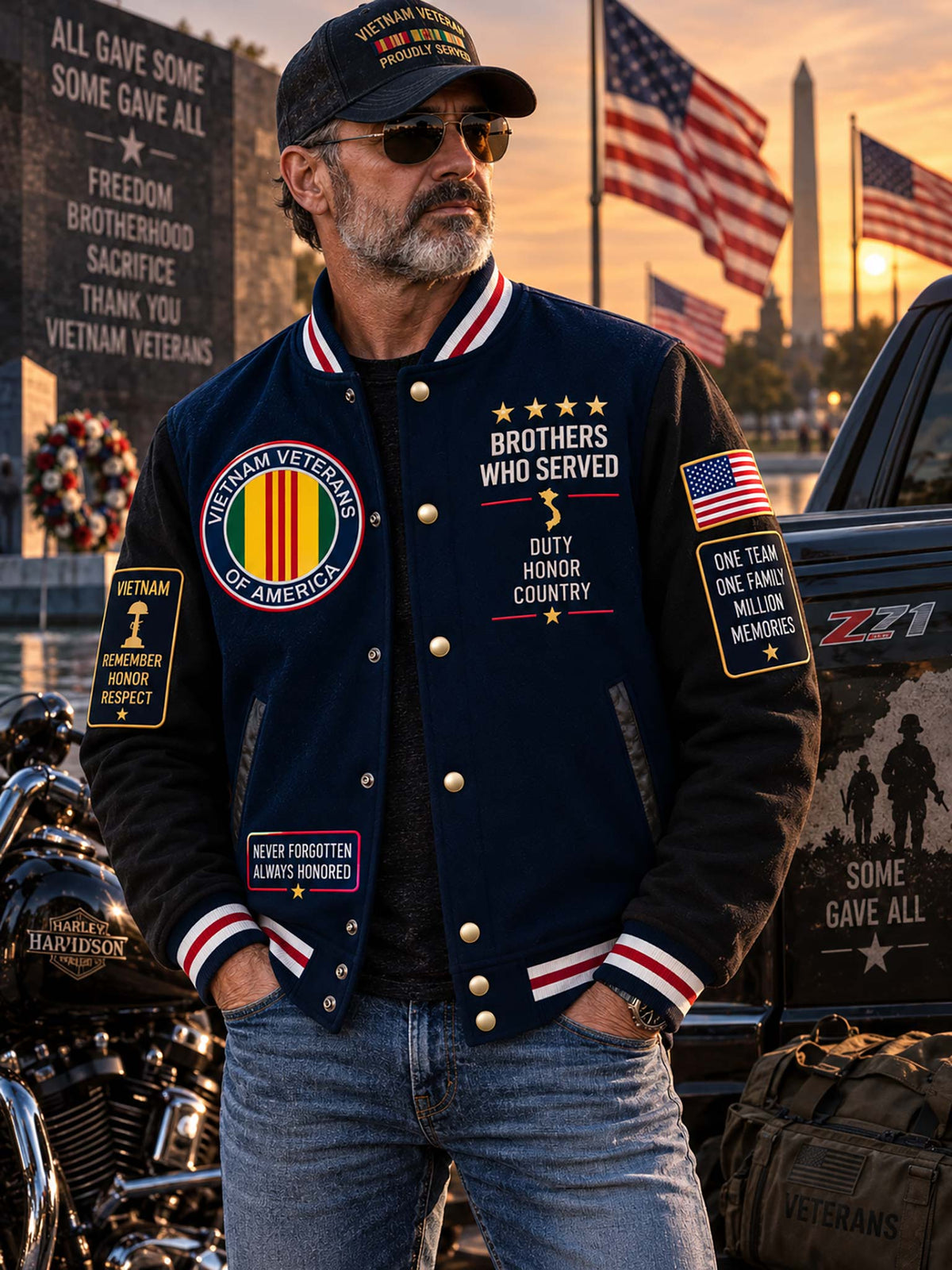 A man wearing a navy blue varsity bomber jacket with military-themed patches and gold buttons, standing outdoors in front of American flags, a motorcycle, and a pickup truck at sunset.