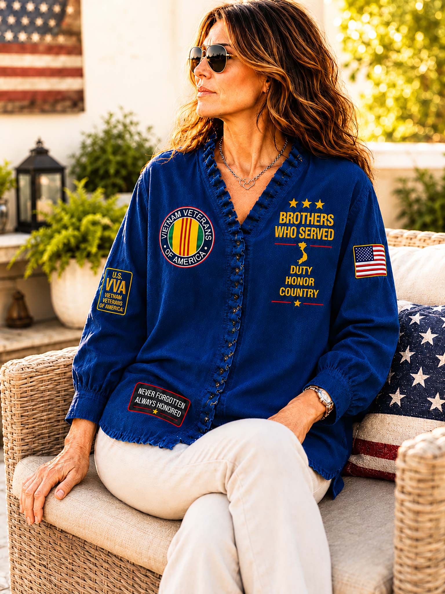 A woman wearing a royal blue button-up shirt with military-style embroidered patches and text, seated on a wicker patio chair outdoors.