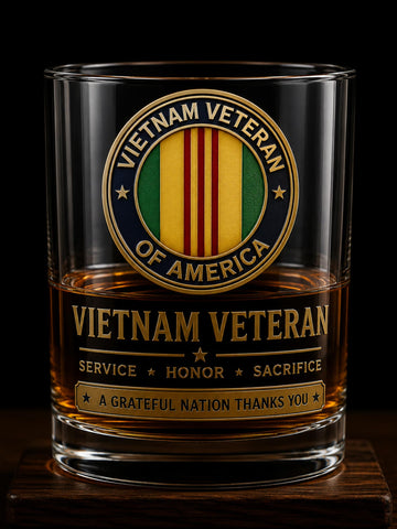 A clear whiskey tumbler with a Vietnam Veteran of America emblem and text printed on the front, filled with amber liquid and photographed against a black background.