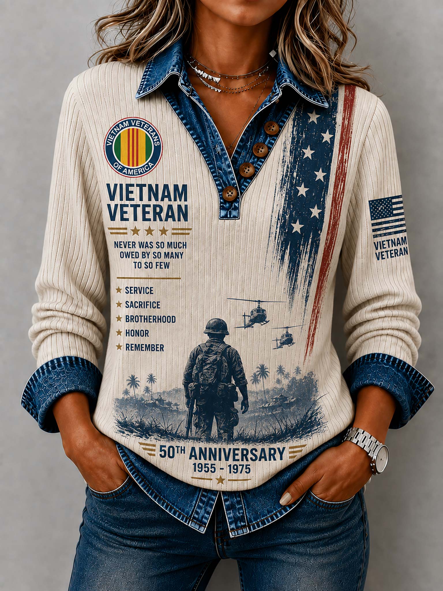 A woman wearing a cream ribbed long-sleeve shirt with a denim collar and cuffs, decorated with a detailed Vietnam Veteran 50th Anniversary graphic print, paired with blue jeans.
