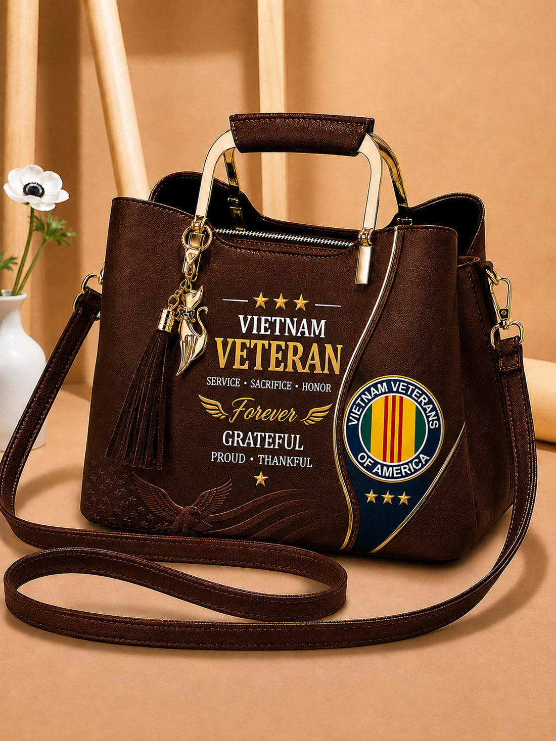 A dark brown faux-leather handbag with a top handle and shoulder strap, featuring a 'Vietnam Veteran' graphic print on the front, a tassel charm, and a gold-toned metal handle.