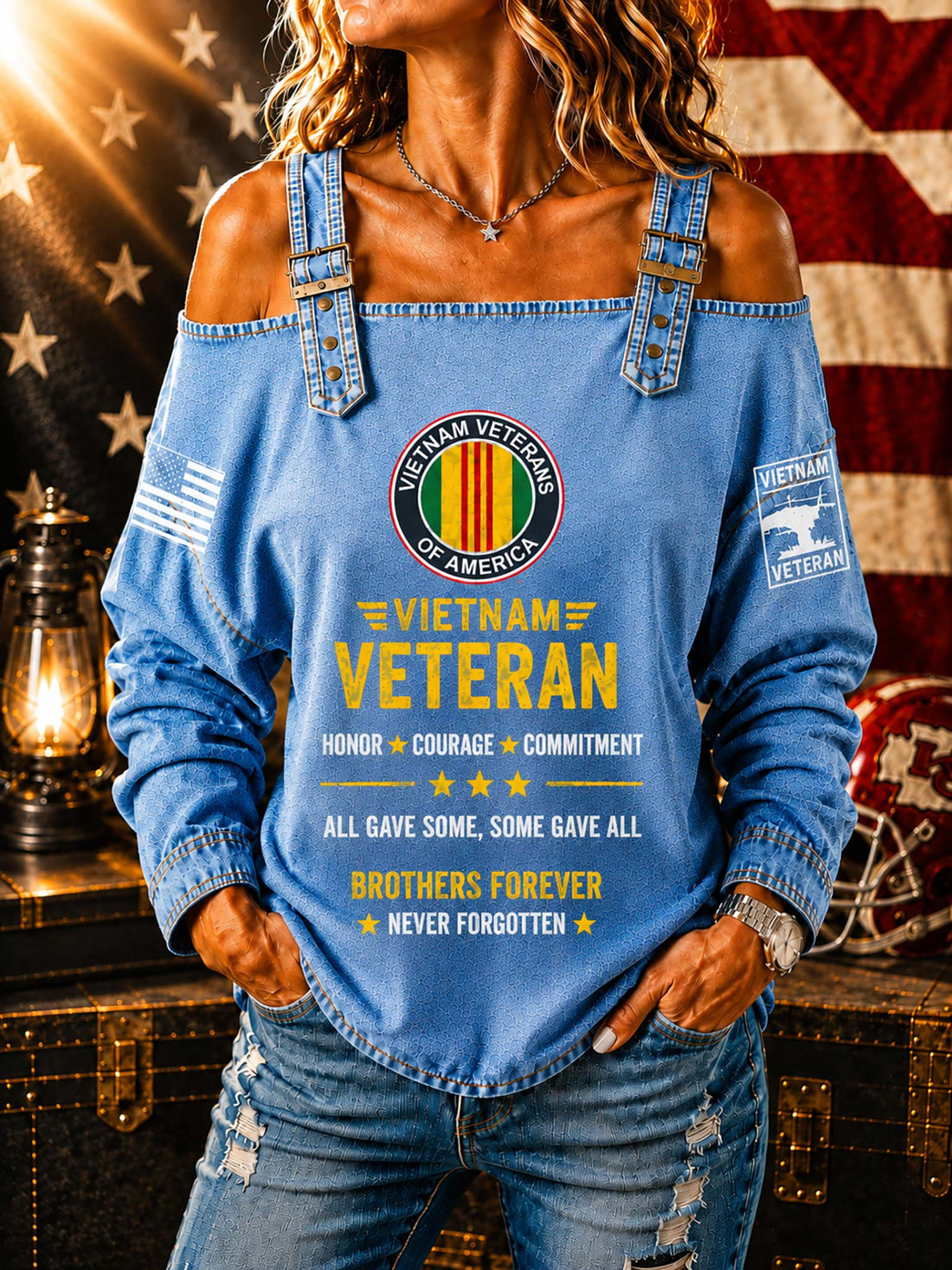 A woman wearing a light blue off-the-shoulder long-sleeve shirt with a distressed denim look. The shirt features a 'Vietnam Veteran of America' emblem on the chest, yellow text reading 'Vietnam Veteran' and 'All gave some, some gave all, brothers forever never forgotten', a small American flag on one sleeve, and a 'Vietnam Veteran' patch on the other sleeve.