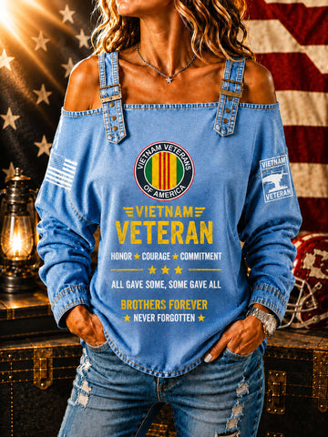 A woman wearing a light blue off-the-shoulder long-sleeve shirt with a distressed denim look. The shirt features a 'Vietnam Veteran of America' emblem on the chest, yellow text reading 'Vietnam Veteran' and 'All gave some, some gave all, brothers forever never forgotten', a small American flag on one sleeve, and a 'Vietnam Veteran' patch on the other sleeve.