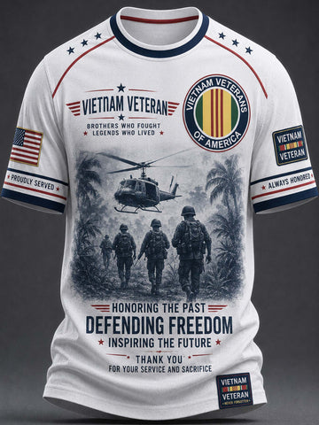 A white short-sleeve t-shirt with a detailed graphic print celebrating Vietnam Veterans. The design features a black-and-white illustration of soldiers and a helicopter, alongside patriotic red, white, and blue ribbons, stars, and text including 'VIETNAM VETERAN' and 'DEFENDING FREEDOM'.
