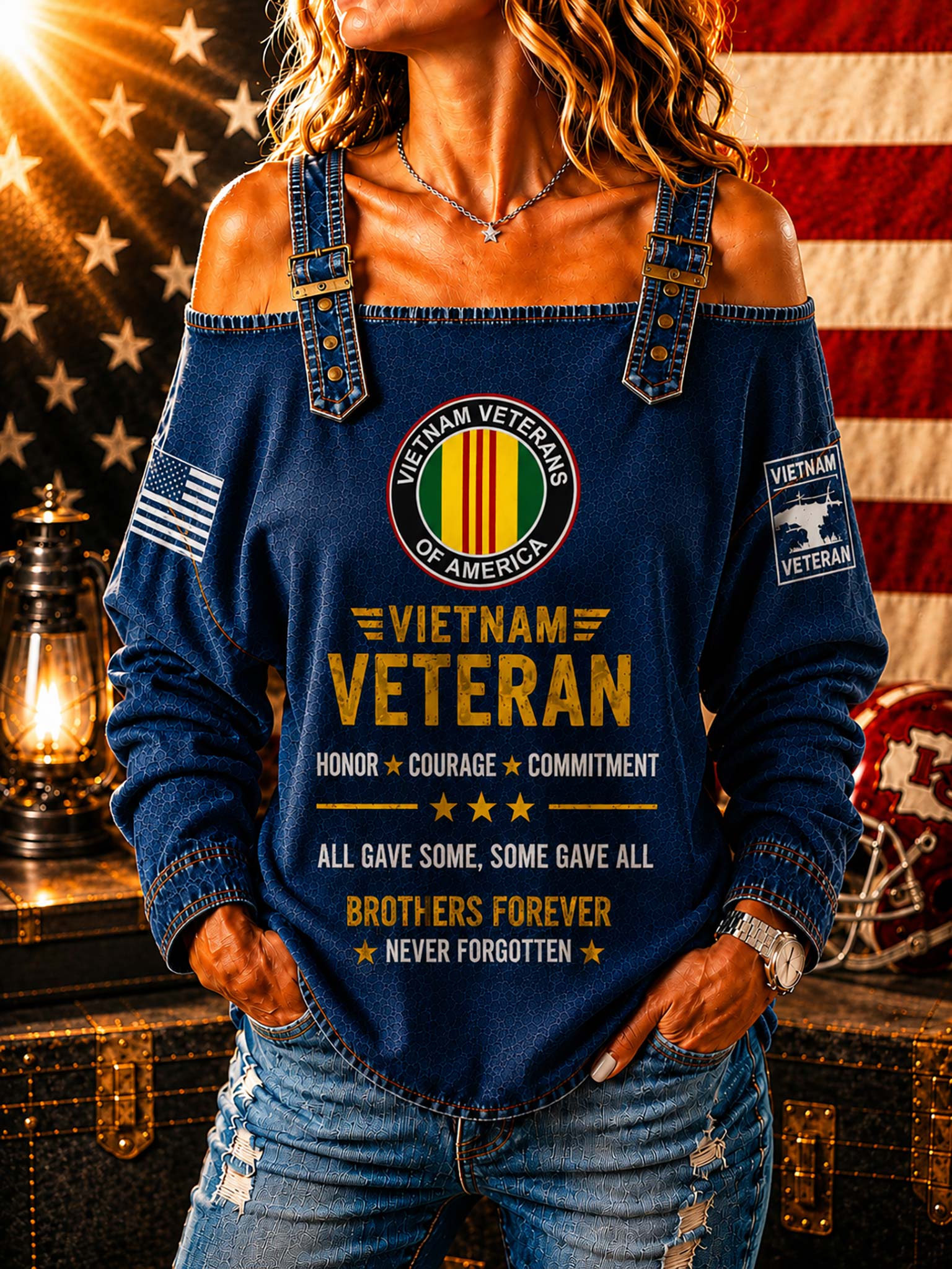 A woman wearing a dark blue off-the-shoulder long-sleeve top with a 'Vietnam Veteran' graphic print on the front, styled with distressed blue jeans in a patriotic setting with an American flag and a lantern.