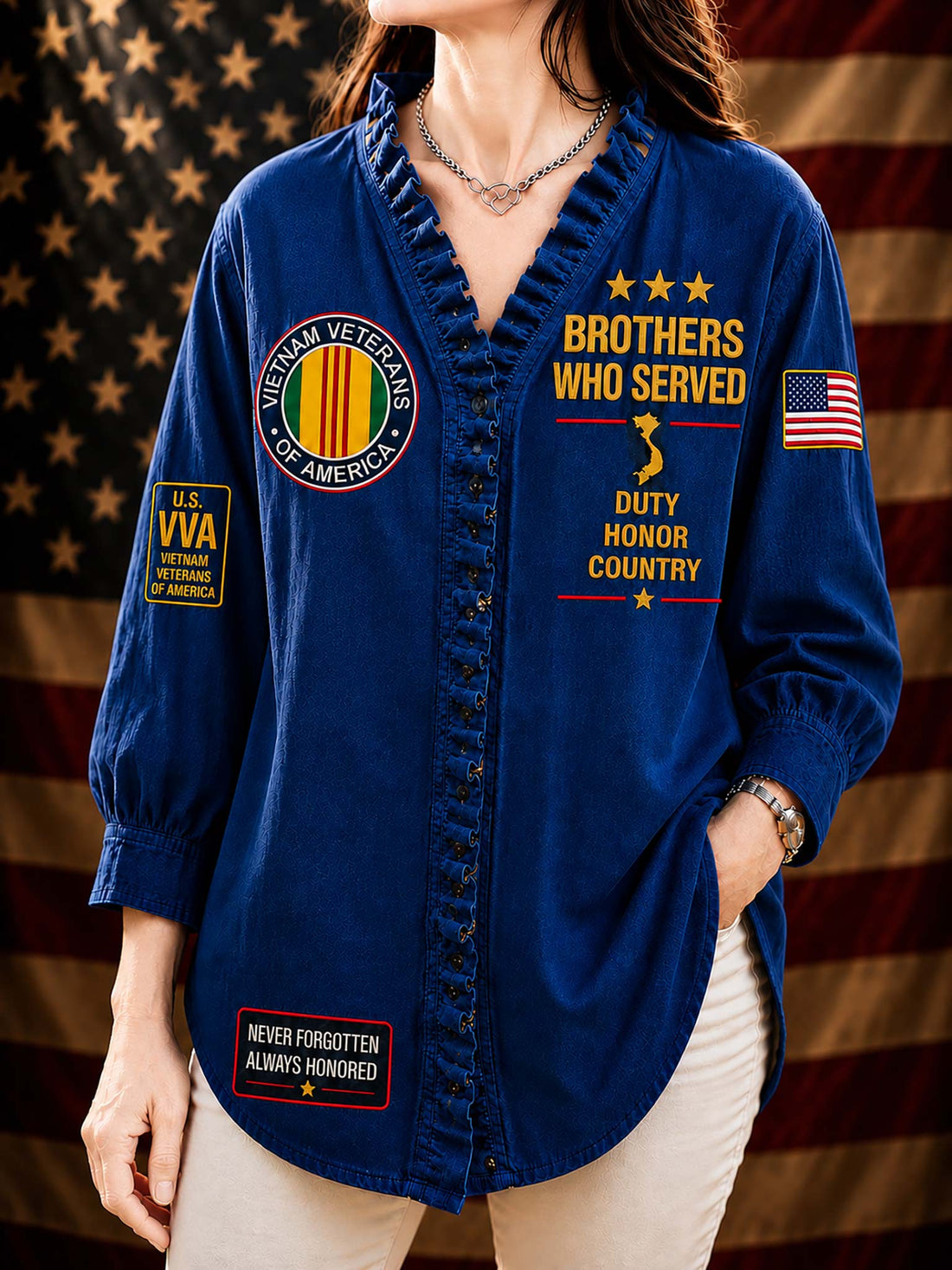 A woman wearing a black long-sleeve button-front shirt with patriotic military-themed graphics, including 'Brothers Who Served,' 'Veterans of America,' and an American flag patch, posed against a blurred American flag background.