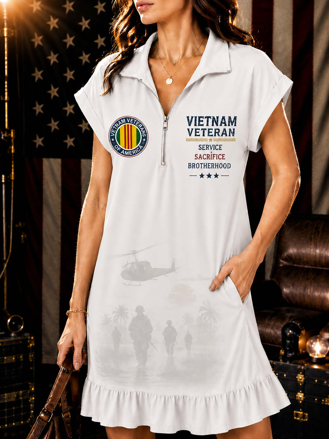 A woman models a white short-sleeve collared dress with a front zipper, 'VIETNAM VETERAN' text, a military emblem, and faint military silhouettes on a ruffled hem, set against a dark patriotic background.