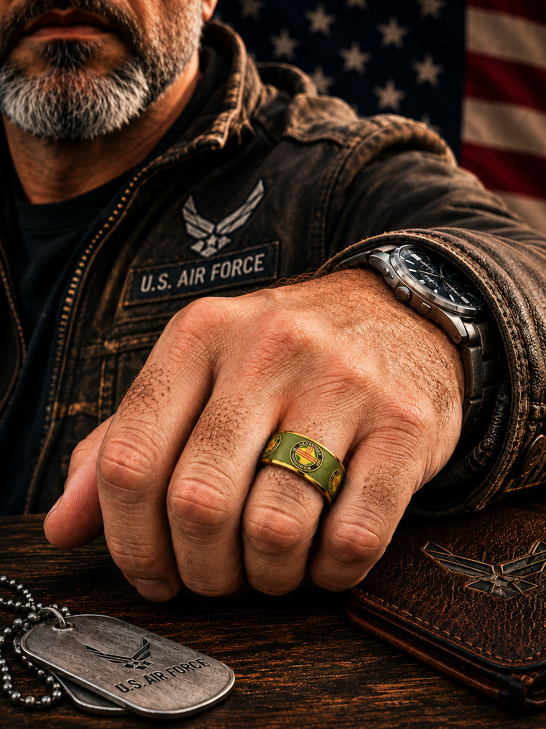 Two interlocking Vietnam Veterans of America rings with a brushed olive green exterior, gold trim, and a silver inner band, set against a blurred American flag background.