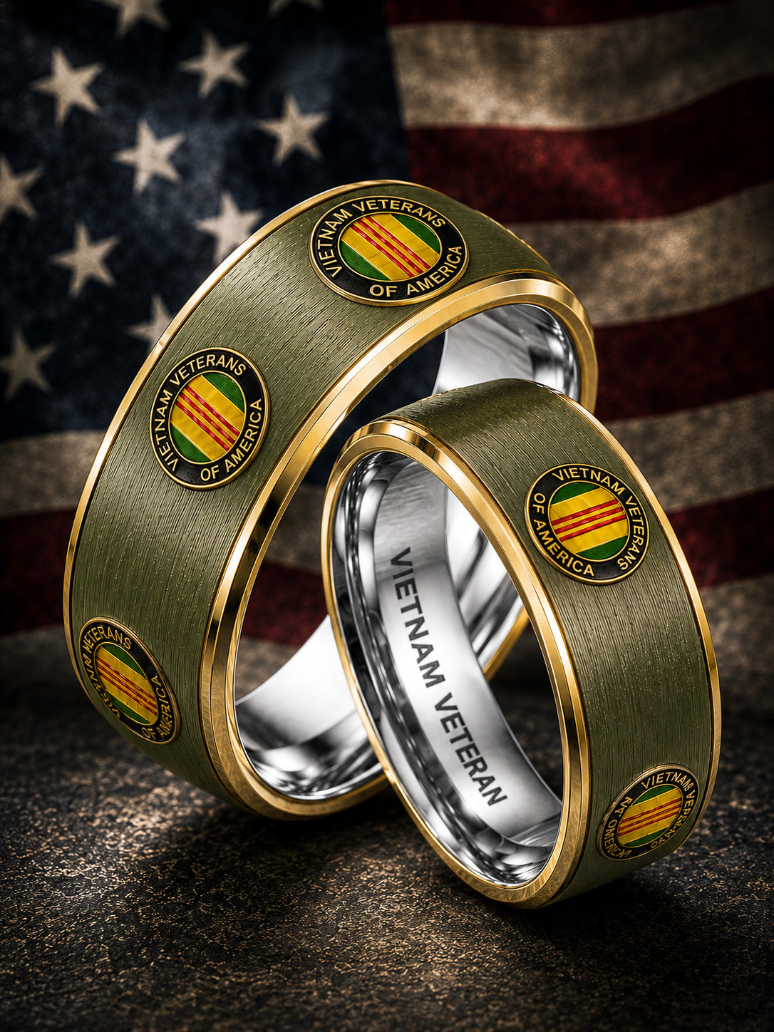 Two interlocking Vietnam Veterans of America rings with a brushed olive green exterior, gold trim, and a silver inner band, set against a blurred American flag background.