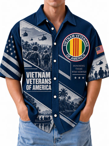 A man wearing a navy blue short-sleeve button-up shirt with a detailed Vietnam Veterans of America graphic print, paired with light blue jeans against a plain white background.