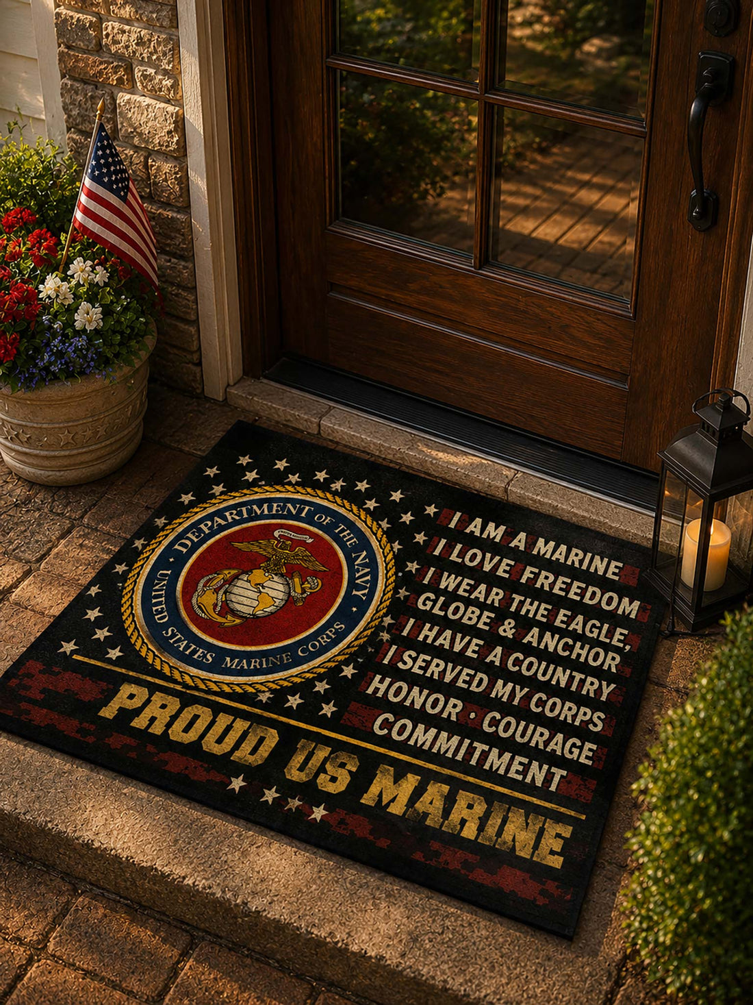 A rectangular doormat placed at a doorway, featuring the United States Marine Corps emblem on the left and printed text reading 'I AM A MARINE', 'I LOVE FREEDOM', 'I WEAR THE EAGLE, GLOBE & ANCHOR', 'I HAVE A COUNTRY', 'I SERVED MY CORPS', 'HONOR, COURAGE', and 'COMMITMENT', with 'PROUD US MARINE' across the bottom. The mat is shown in a real entryway setting with wood flooring, glass doors, and a small flower arrangement.