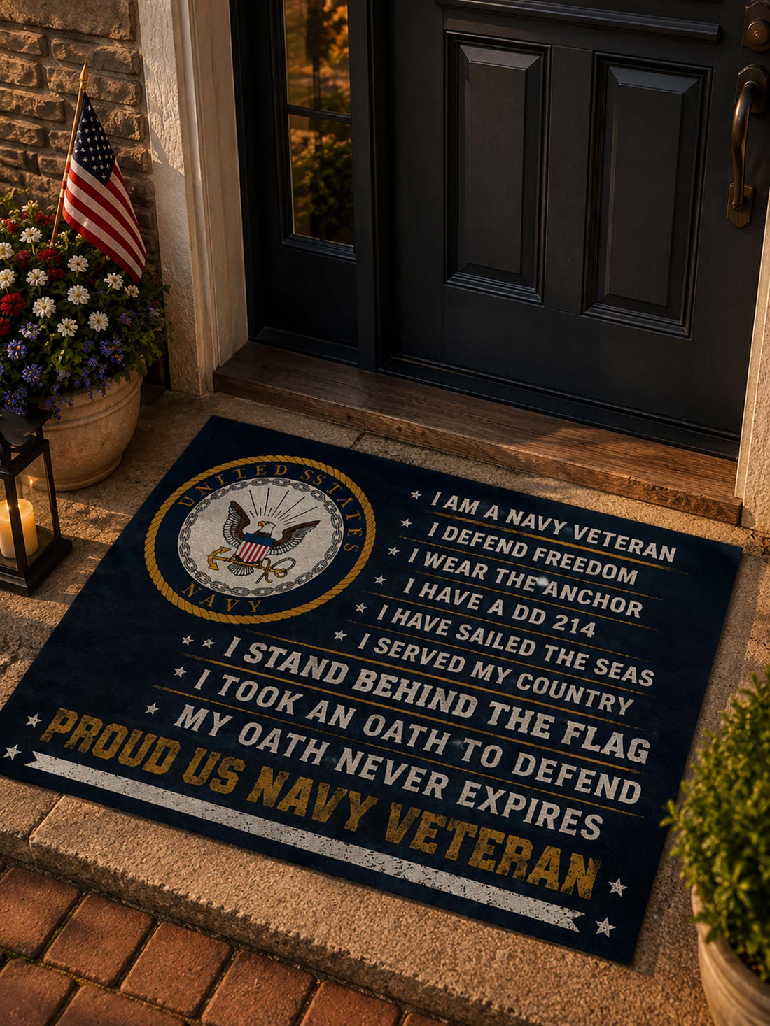 A navy blue doormat with a United States Navy emblem and patriotic text, placed on a tan entryway step in front of a glass door.