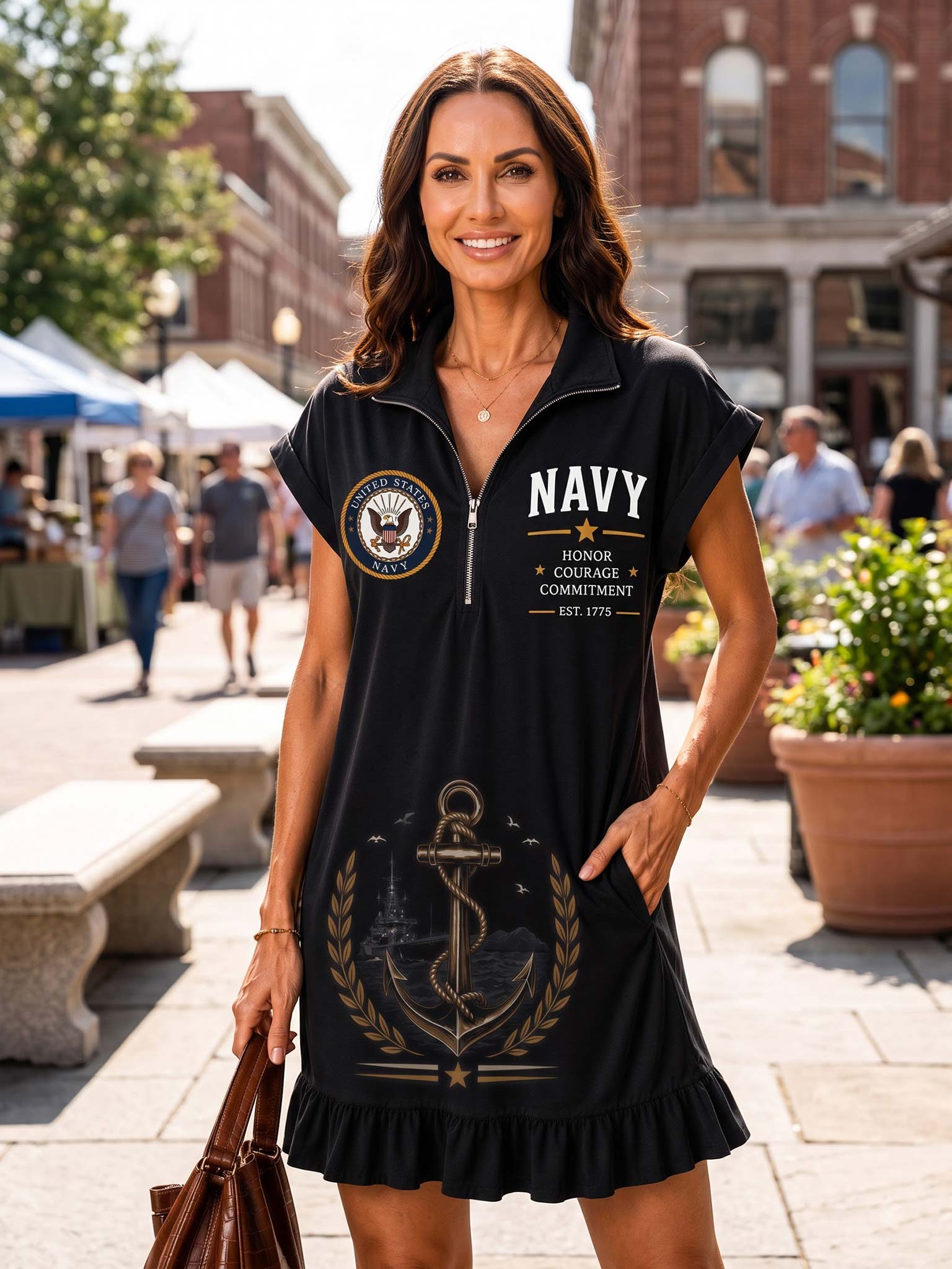 A woman modeling a black short-sleeve zip-front dress with a ruffled hem in an outdoor urban plaza. The dress features a white and gold 'NAVY' print on the chest, a circular military-style emblem on the left chest, and a large gold anchor and laurel wreath graphic on the front.