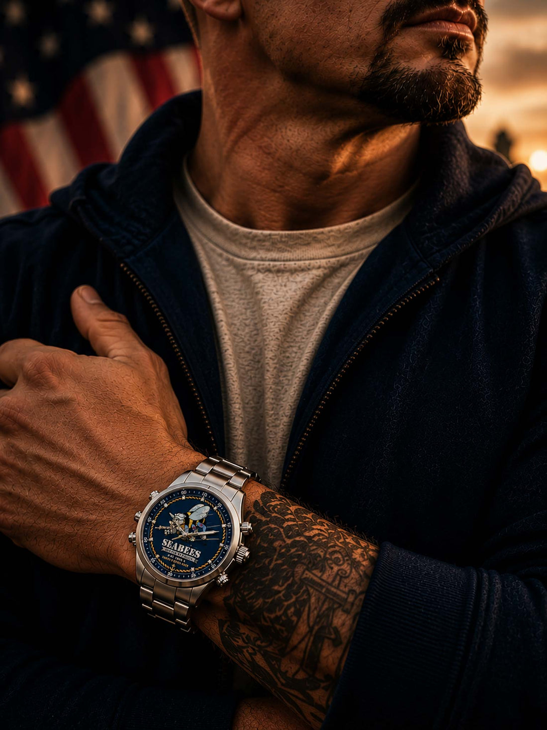 A stainless steel wristwatch with a blue Seabees dial featuring a cartoon bee and the text 'SEABEES WE BUILD WE FIGHT EST. 1942 UNITED STATES NAVY,' shown on a wooden surface with an American flag background.