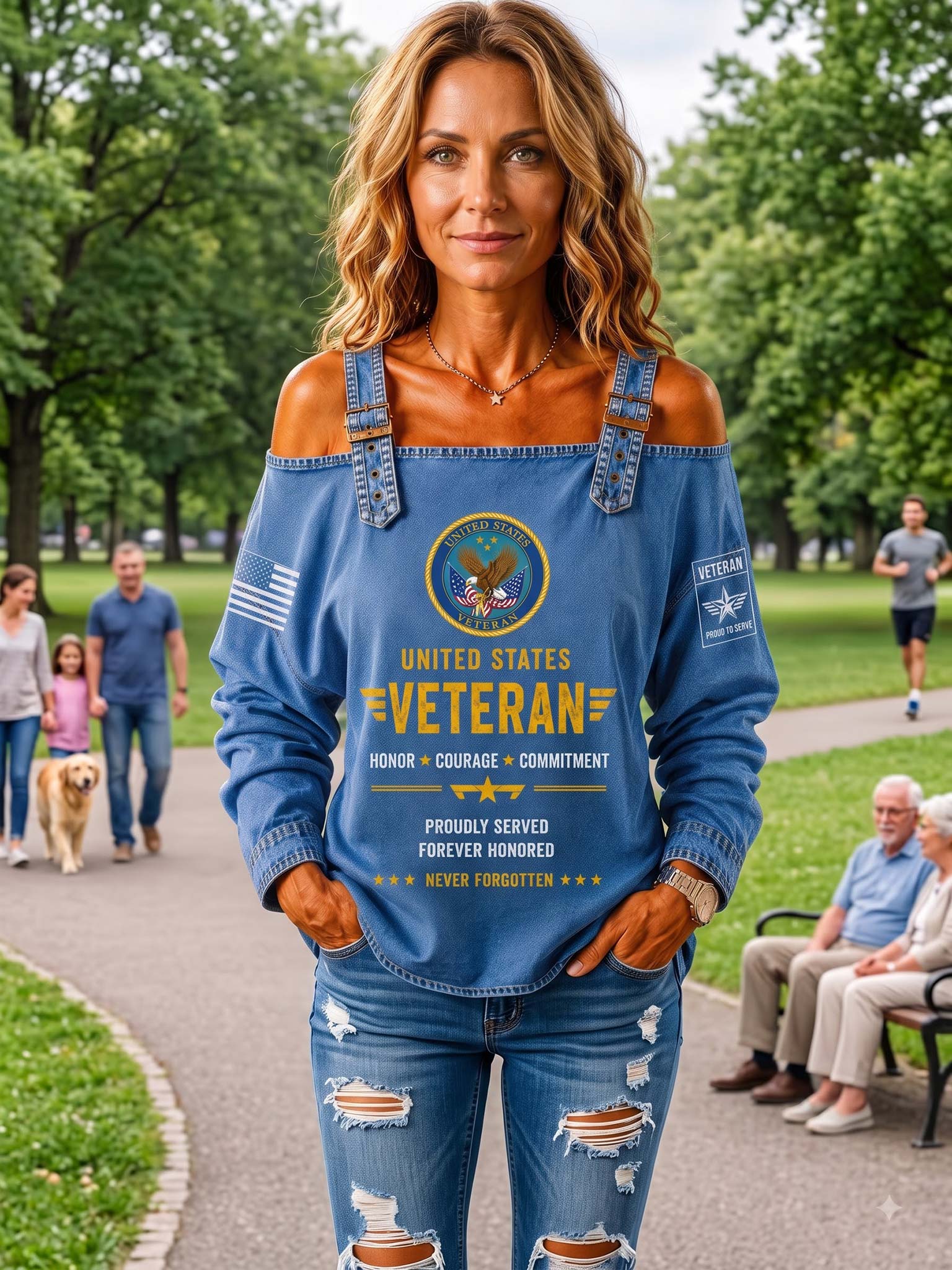 A woman standing in a park wearing a blue off-the-shoulder long-sleeve top with distressed denim-style sleeves and a large patriotic veteran graphic on the front, paired with matching distressed blue jeans.