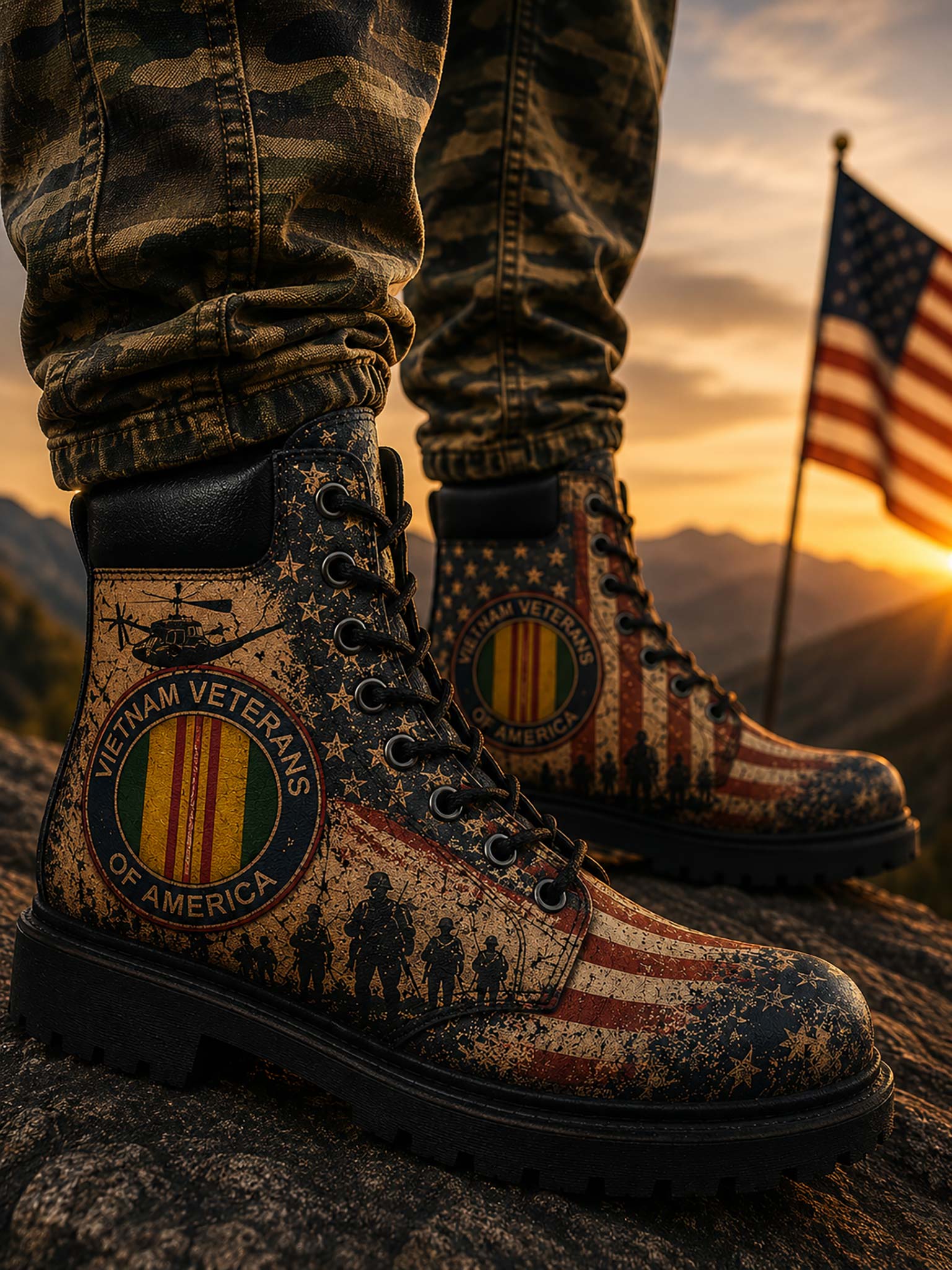 Close-up of a person wearing camouflage pants and military-style boots with a distressed American flag and Vietnam Veterans emblem, standing outdoors at sunset with mountains and a flag in the background.
