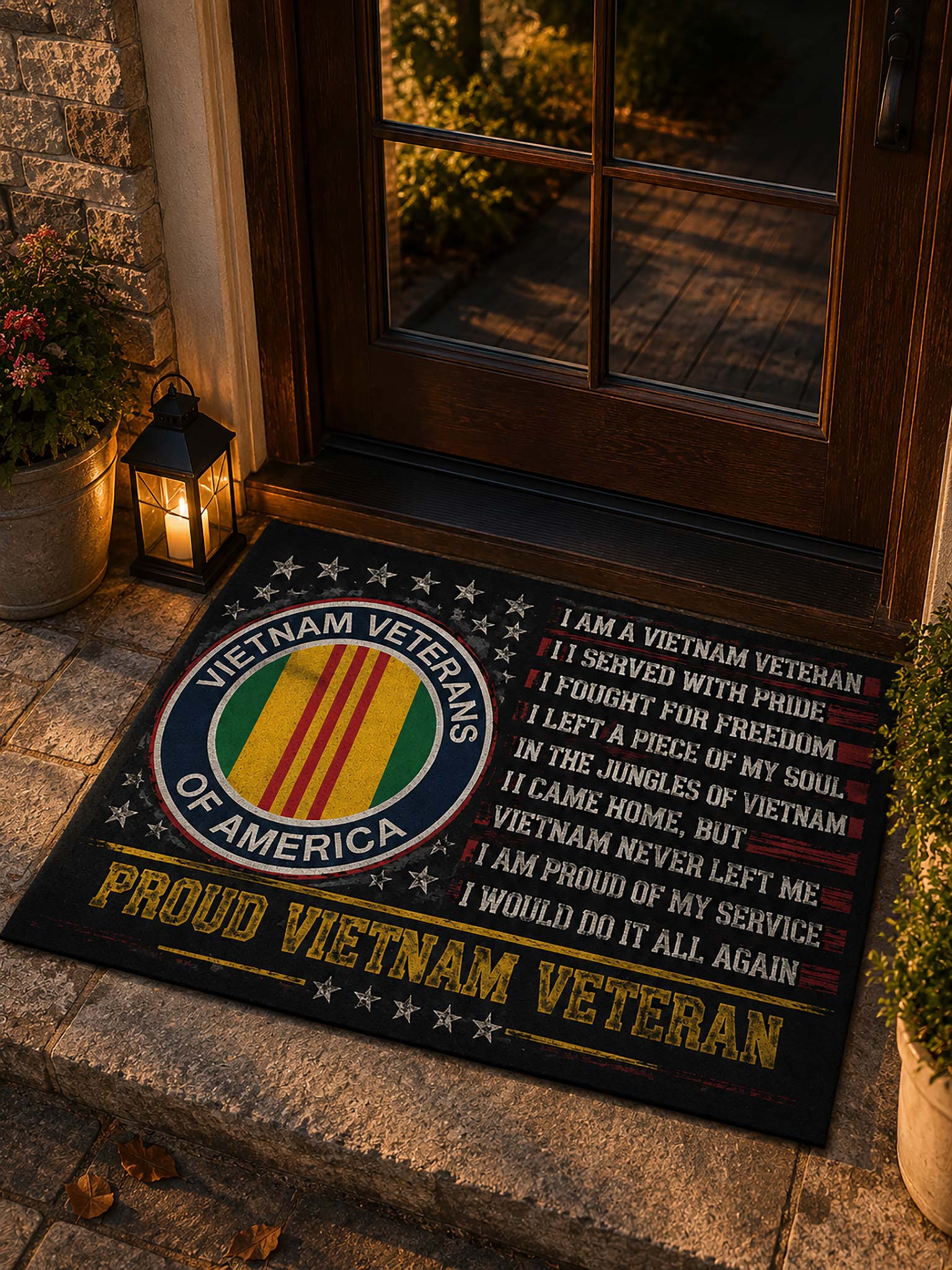 A rectangular black doormat with a Vietnam Veterans design, placed in front of a wooden front door on stone steps. The mat features a circular Vietnam Veterans emblem with red, yellow, green, and white stripes, white stars, and a printed patriotic quote in white and yellow text.